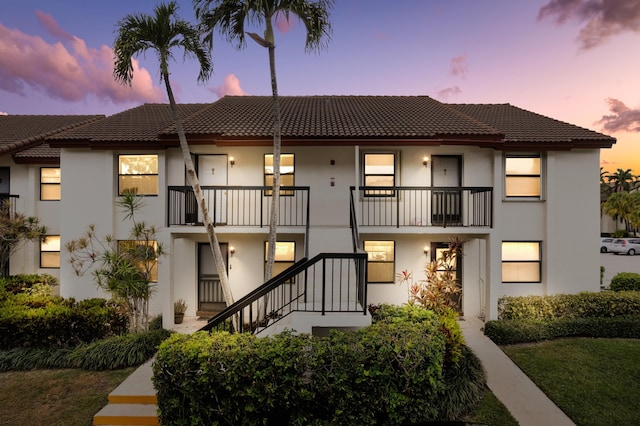 back of house at dusk with stairs, a tiled roof, and stucco siding