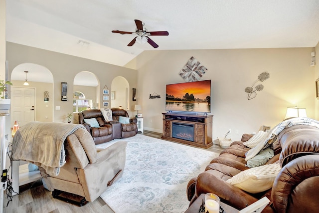 living area with arched walkways, visible vents, light wood-style flooring, a glass covered fireplace, and vaulted ceiling