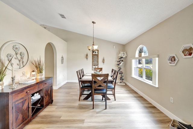 dining room featuring arched walkways, lofted ceiling, visible vents, light wood-style flooring, and baseboards