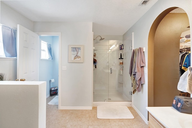 bathroom featuring a spacious closet, a stall shower, visible vents, and baseboards