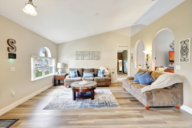 living room with light wood finished floors, visible vents, arched walkways, baseboards, and lofted ceiling