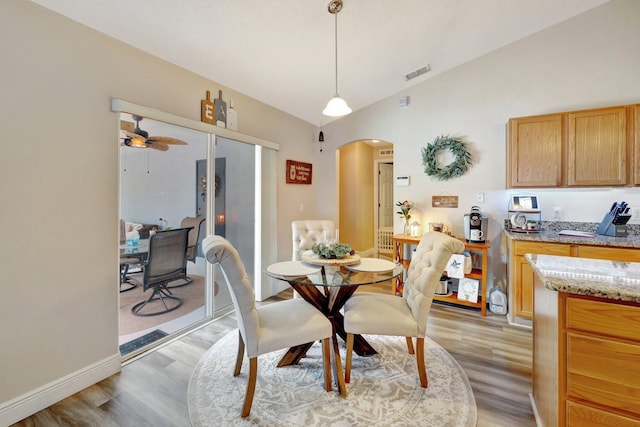 dining space featuring arched walkways, visible vents, light wood-style floors, vaulted ceiling, and baseboards