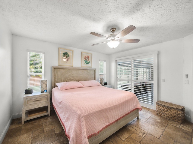 bedroom with stone tile floors, baseboards, ceiling fan, and a textured ceiling