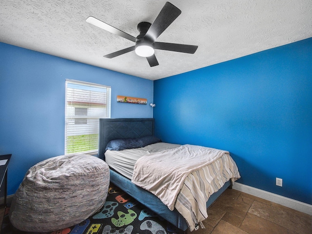 bedroom featuring baseboards, ceiling fan, a textured ceiling, and stone tile floors