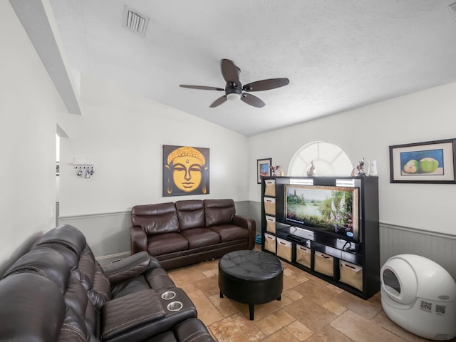 living room with visible vents, a wainscoted wall, stone finish flooring, vaulted ceiling, and a textured ceiling