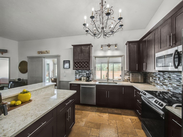 kitchen with appliances with stainless steel finishes, stone tile flooring, a sink, and decorative backsplash