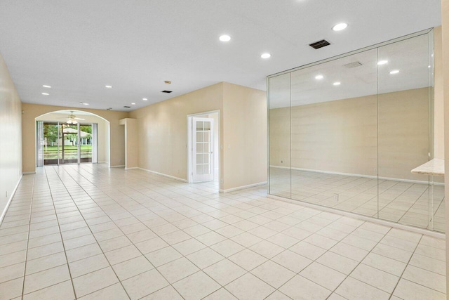 empty room featuring arched walkways, light tile patterned floors, recessed lighting, and visible vents