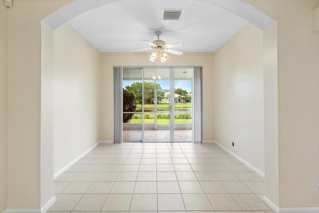 unfurnished room with baseboards, visible vents, light tile patterned flooring, arched walkways, and ceiling fan