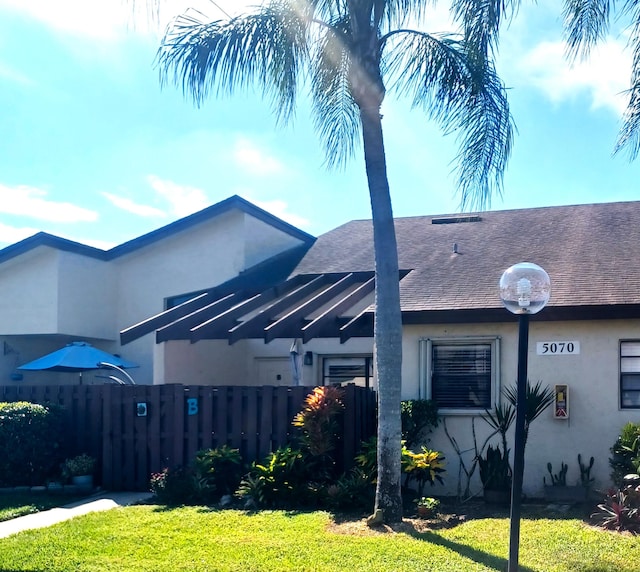 view of side of home featuring stucco siding, a lawn, roof with shingles, and fence