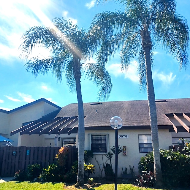 back of property featuring a shingled roof, fence, and stucco siding