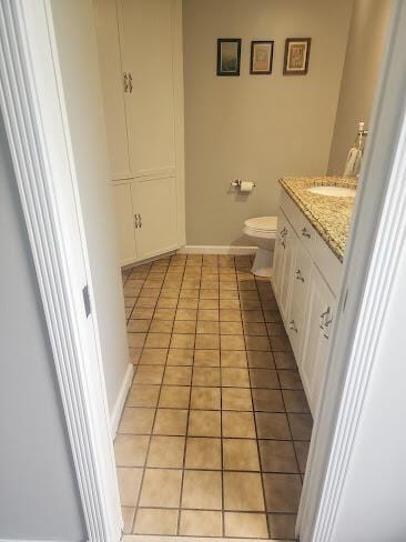 half bath featuring toilet, tile patterned flooring, baseboards, and vanity