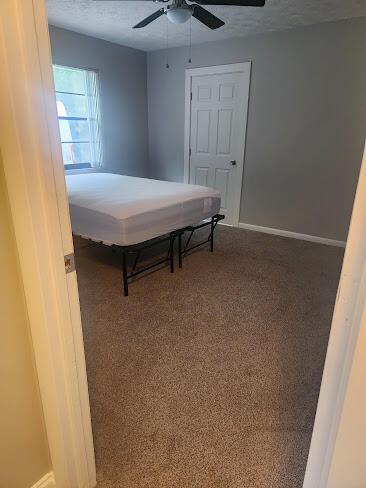 bedroom featuring a textured ceiling, dark colored carpet, ceiling fan, and baseboards