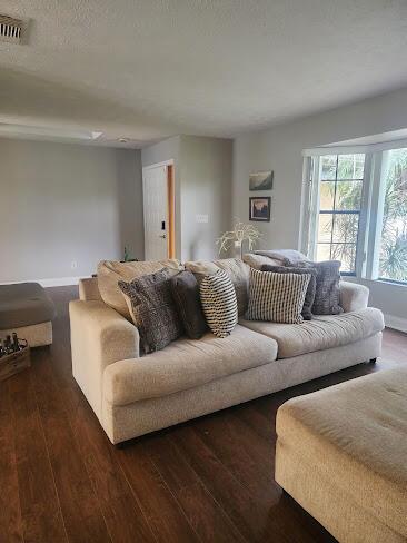 living area with baseboards, a textured ceiling, visible vents, and dark wood-style flooring