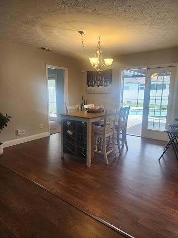 dining area featuring a textured ceiling, dark wood-style flooring, a chandelier, and baseboards