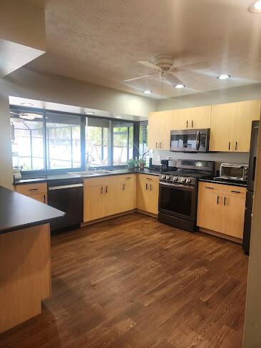 kitchen featuring dark wood-type flooring, dark countertops, black appliances, and light brown cabinetry