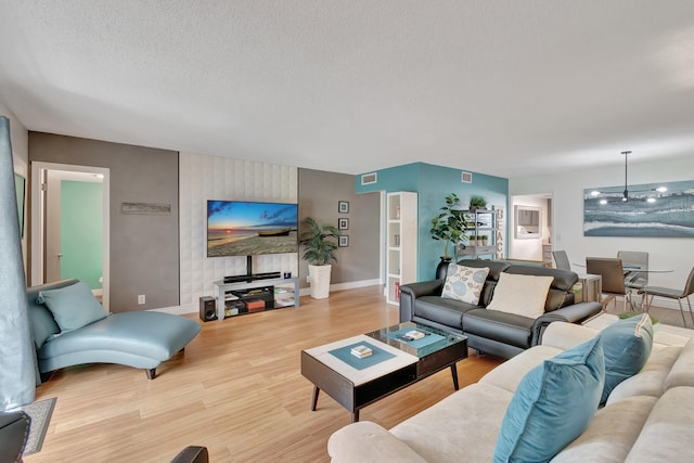 living room with a textured ceiling, wood finished floors, visible vents, and baseboards