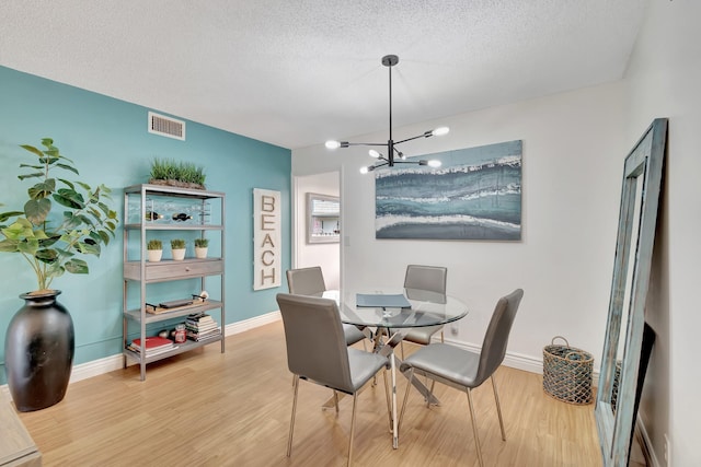 dining room featuring a textured ceiling, wood finished floors, visible vents, and a chandelier