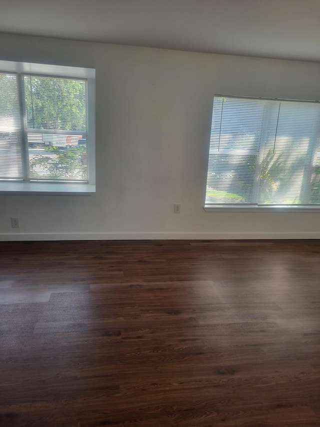 spare room with dark wood-style floors, a healthy amount of sunlight, and baseboards