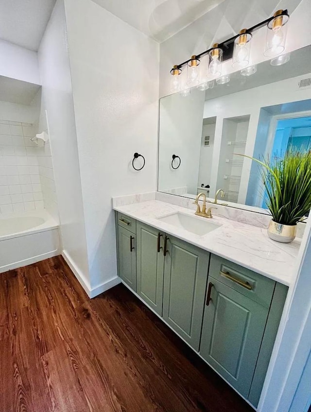 bathroom featuring visible vents, baseboards, wood finished floors, tub / shower combination, and vanity