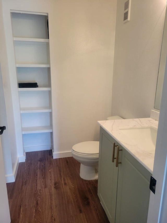 bathroom with toilet, wood finished floors, vanity, baseboards, and a closet