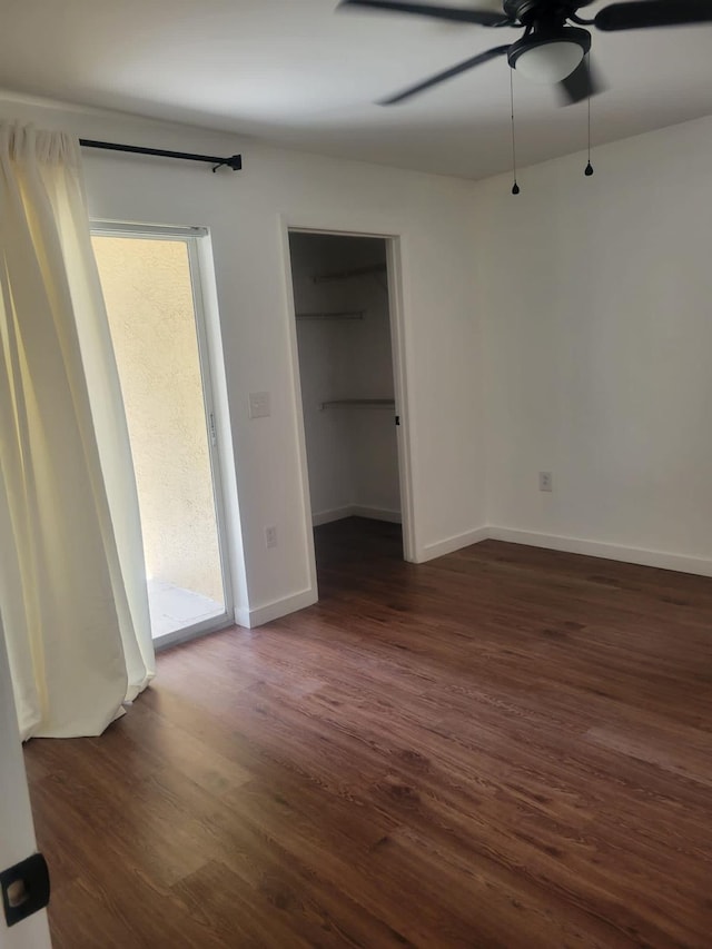 unfurnished bedroom with a ceiling fan, baseboards, a walk in closet, and dark wood-type flooring