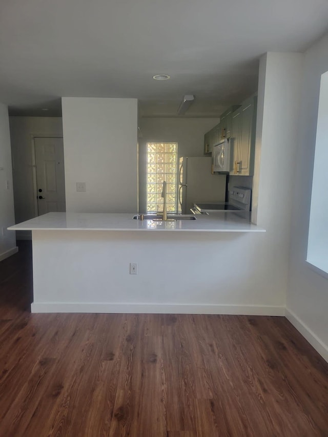 kitchen featuring white appliances, dark wood-type flooring, a peninsula, light countertops, and a sink