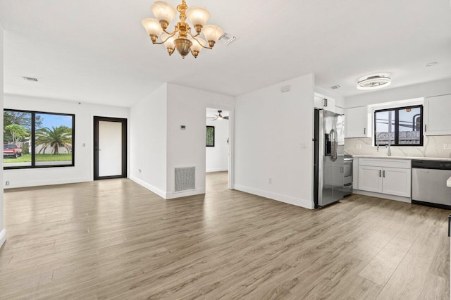 unfurnished living room with light wood-type flooring, a sink, visible vents, and baseboards