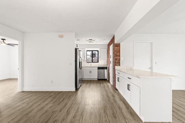 kitchen with stainless steel appliances, white cabinetry, light wood-type flooring, a peninsula, and baseboards