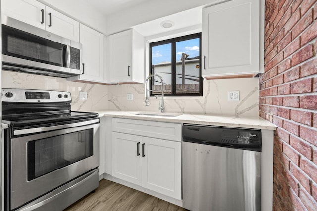 kitchen featuring light stone counters, brick wall, stainless steel appliances, a sink, and white cabinets