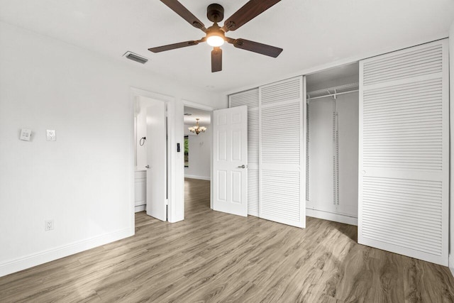 unfurnished bedroom featuring baseboards, visible vents, wood finished floors, a closet, and ceiling fan with notable chandelier