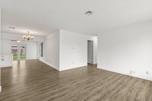 spare room featuring a chandelier, visible vents, baseboards, and wood finished floors