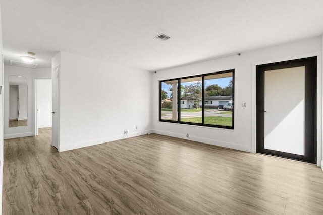 empty room with wood finished floors, visible vents, and baseboards