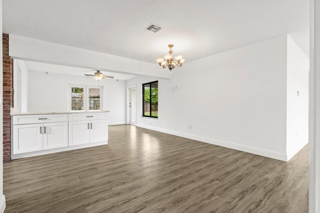 unfurnished living room featuring ceiling fan with notable chandelier, wood finished floors, visible vents, and baseboards