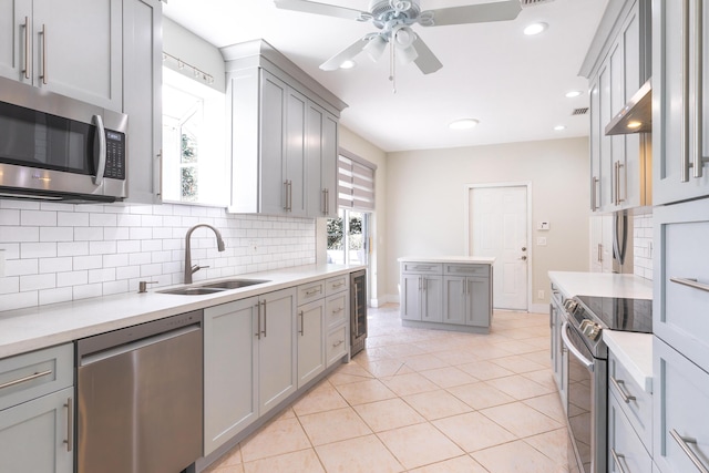 kitchen with gray cabinets, light countertops, decorative backsplash, appliances with stainless steel finishes, and a sink