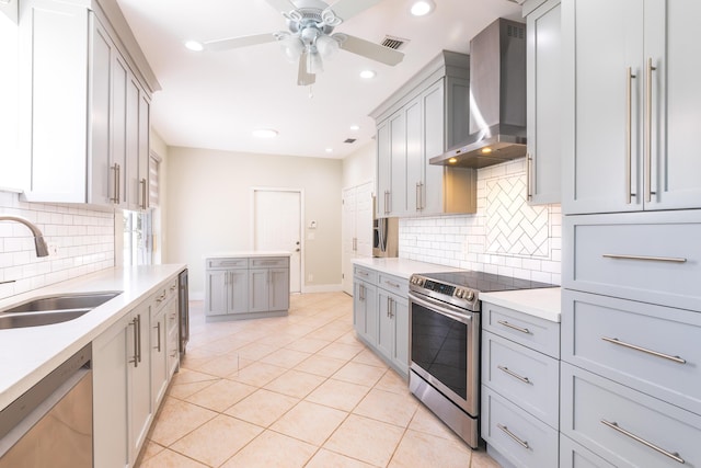 kitchen featuring stainless steel appliances, gray cabinets, light countertops, a sink, and wall chimney exhaust hood