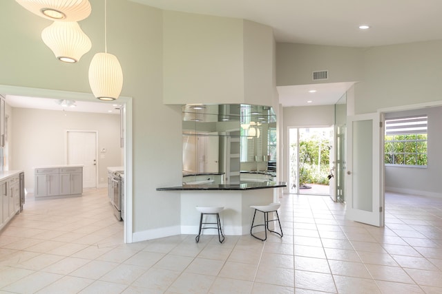 kitchen featuring a breakfast bar, pendant lighting, light tile patterned floors, visible vents, and high vaulted ceiling