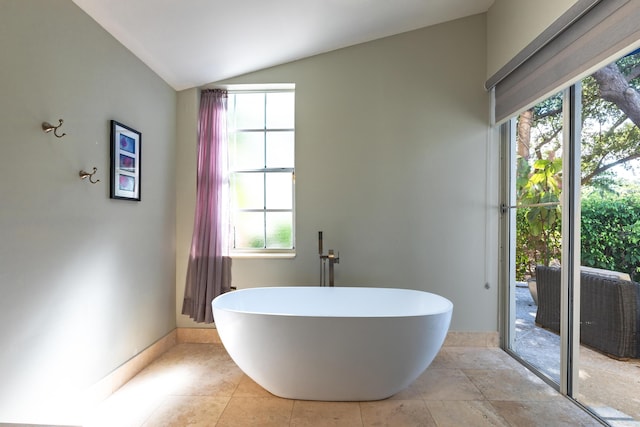 bathroom with lofted ceiling, a soaking tub, tile patterned flooring, and a wealth of natural light