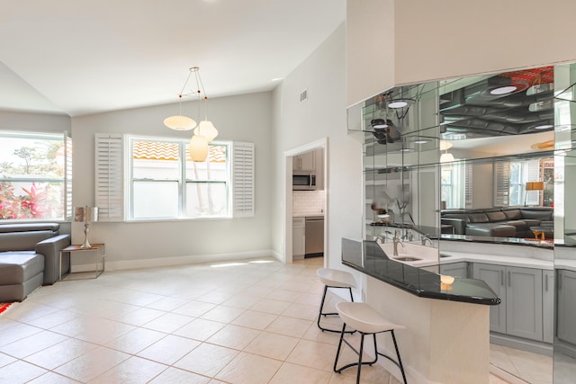 interior space with gray cabinetry, stainless steel appliances, open floor plan, hanging light fixtures, and a kitchen bar