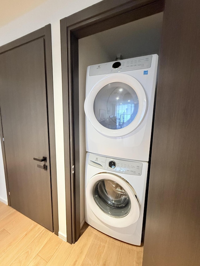 clothes washing area featuring stacked washer and dryer, laundry area, and wood finished floors