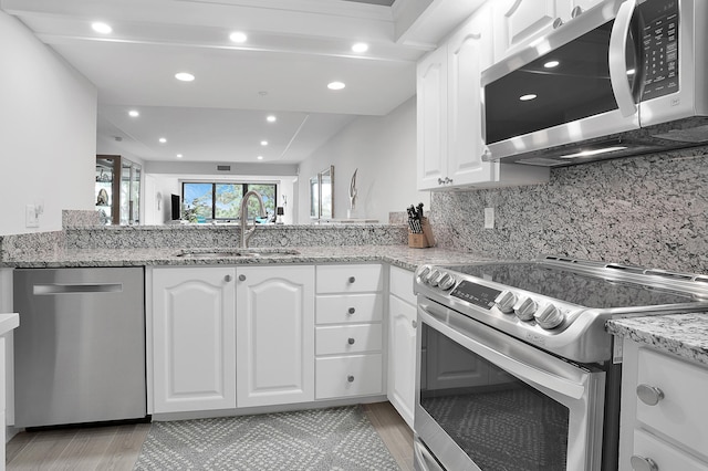 kitchen with light stone countertops, appliances with stainless steel finishes, white cabinets, and a sink