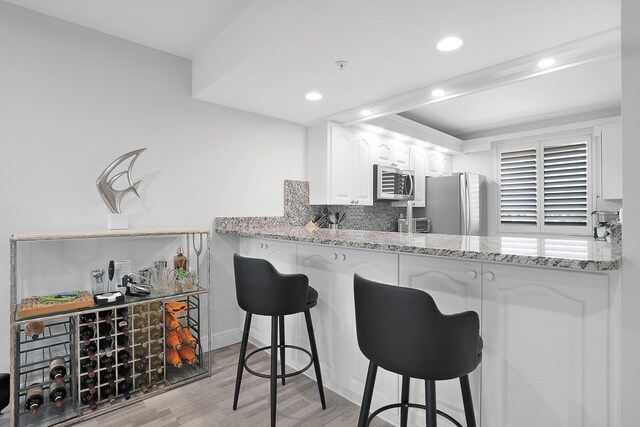 kitchen with light wood finished floors, stainless steel appliances, white cabinetry, decorative backsplash, and light stone counters