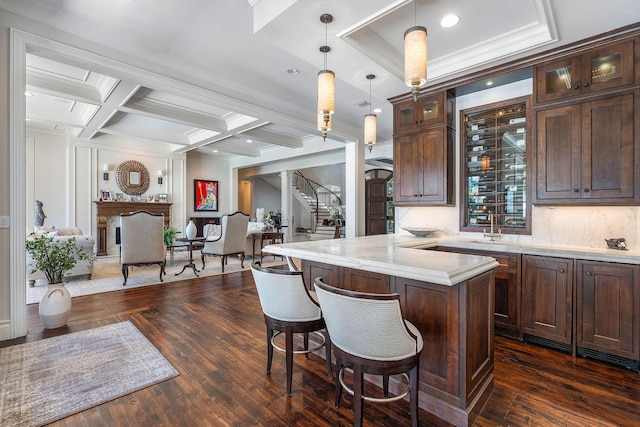 kitchen featuring dark wood-type flooring, dark brown cabinets, a breakfast bar area, and coffered ceiling