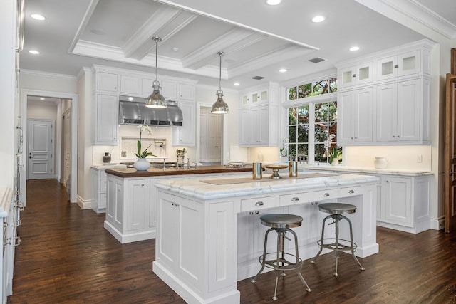 kitchen with visible vents, a kitchen island, ornamental molding, white cabinets, and glass insert cabinets