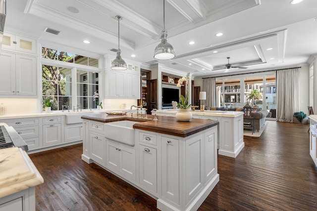 kitchen featuring visible vents, wooden counters, an island with sink, a sink, and open floor plan