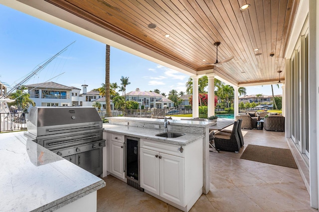 view of patio / terrace featuring beverage cooler, a sink, a residential view, exterior kitchen, and ceiling fan