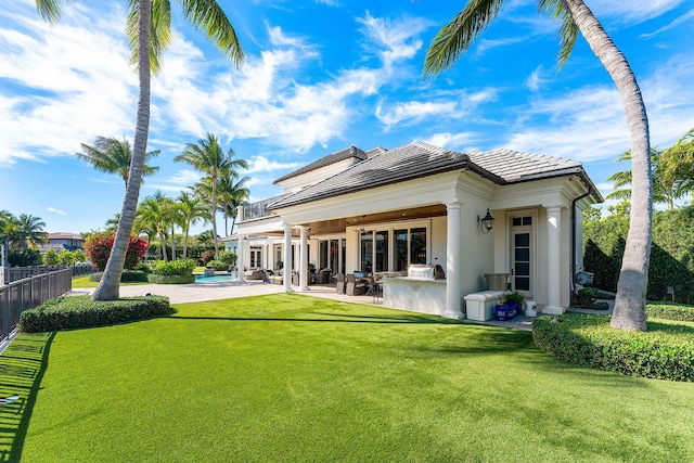 rear view of property with fence, a tiled roof, stucco siding, a yard, and a patio