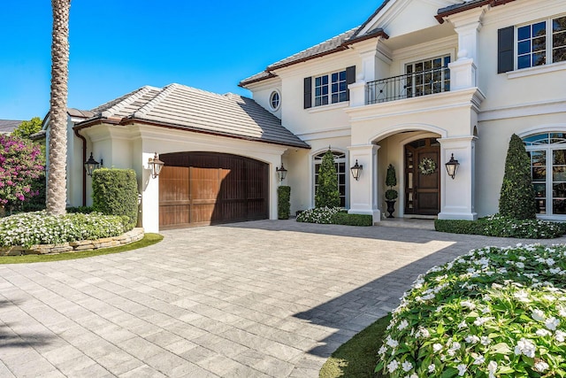 mediterranean / spanish home featuring decorative driveway, a balcony, an attached garage, and stucco siding