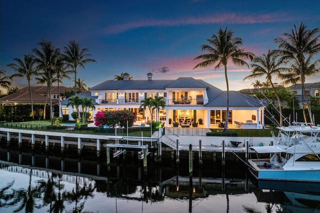 back of house at dusk featuring a patio area, boat lift, a balcony, and a water view