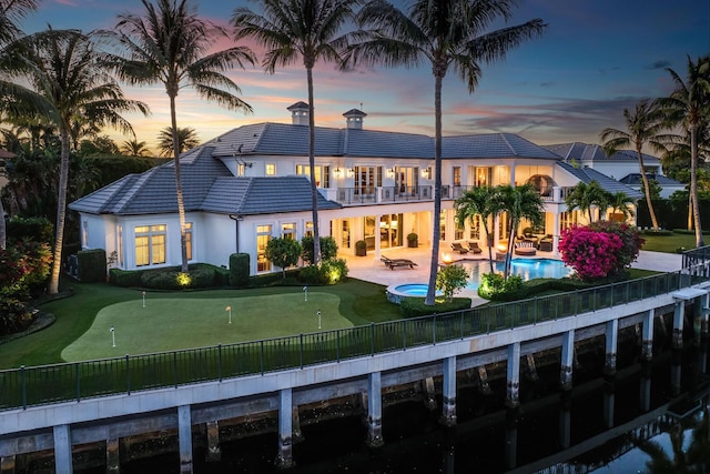 back of property at dusk with a patio, a balcony, a pool with connected hot tub, stucco siding, and a tile roof