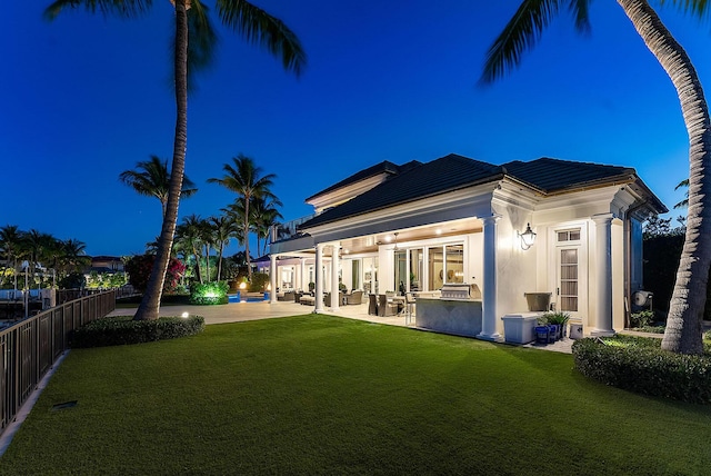 rear view of property with fence, exterior kitchen, a yard, stucco siding, and a patio area